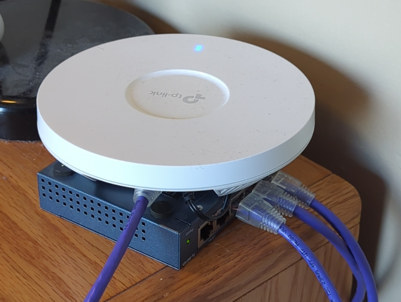 an ethernet switch with 3 cables plugged into it. 1 of them plugs into a circular white TP-Link device with a solid blue LED.